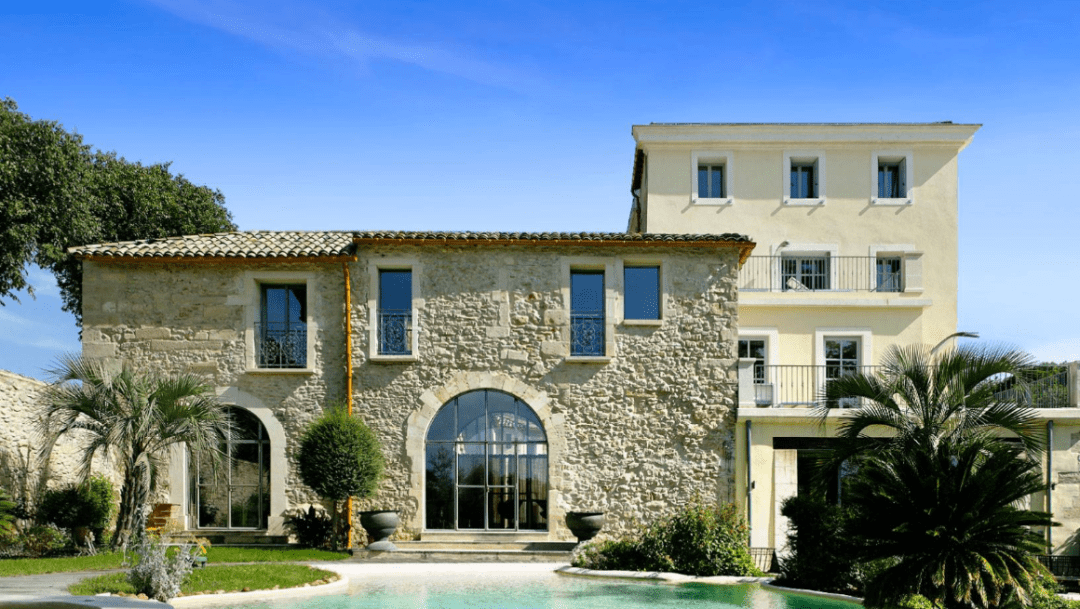 A large stone house with a pool at the front. The rustic and elegant architecture of the house blends harmoniously with the outdoor setting, creating a warm and welcoming atmosphere.