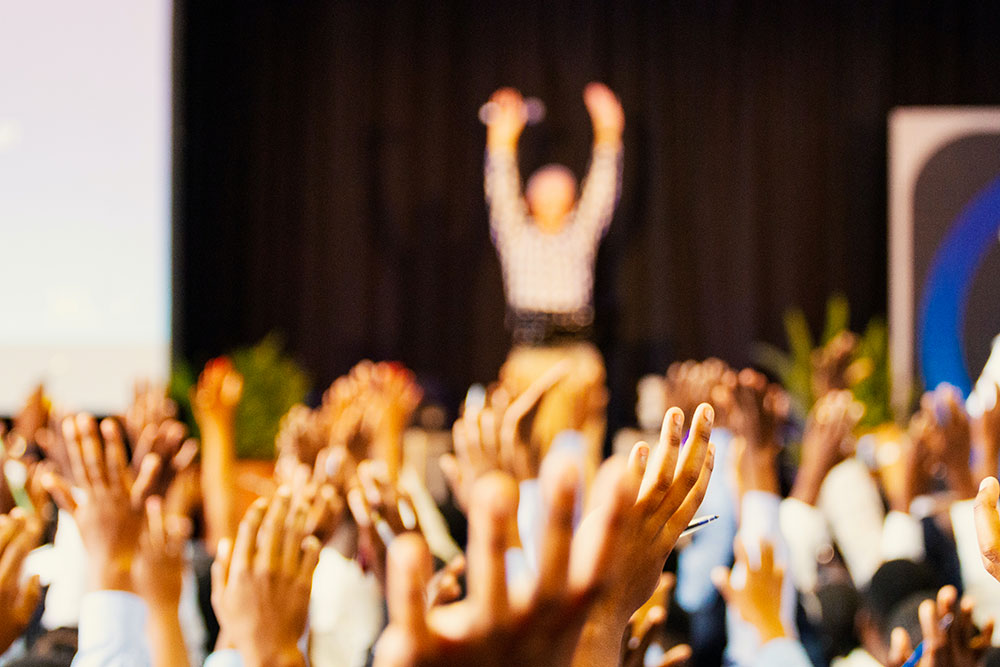 A crowd raises their arms in front of a speaker. - Eventdrive Blog Article