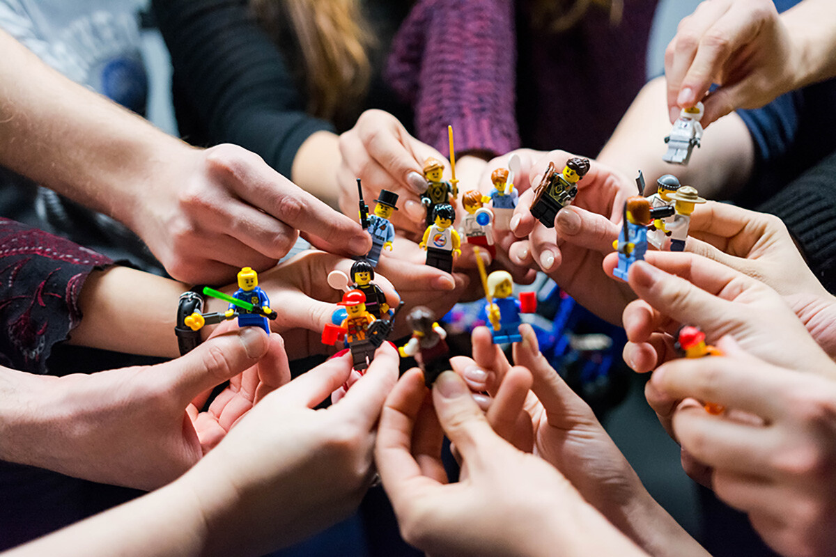 Un groupe de personnes tient des figurines LEGO, formant un cercle avec leurs mains. Les figurines représentent divers personnages et sont tenues de manière collaborative, symbolisant un travail d'équipe ou un moment ludique partagé. - Article de blog Eventdrive