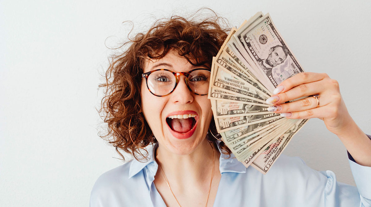 Smiling woman wearing glasses and holding a fan of American banknotes in her hand. - Eventdrive Blog Article