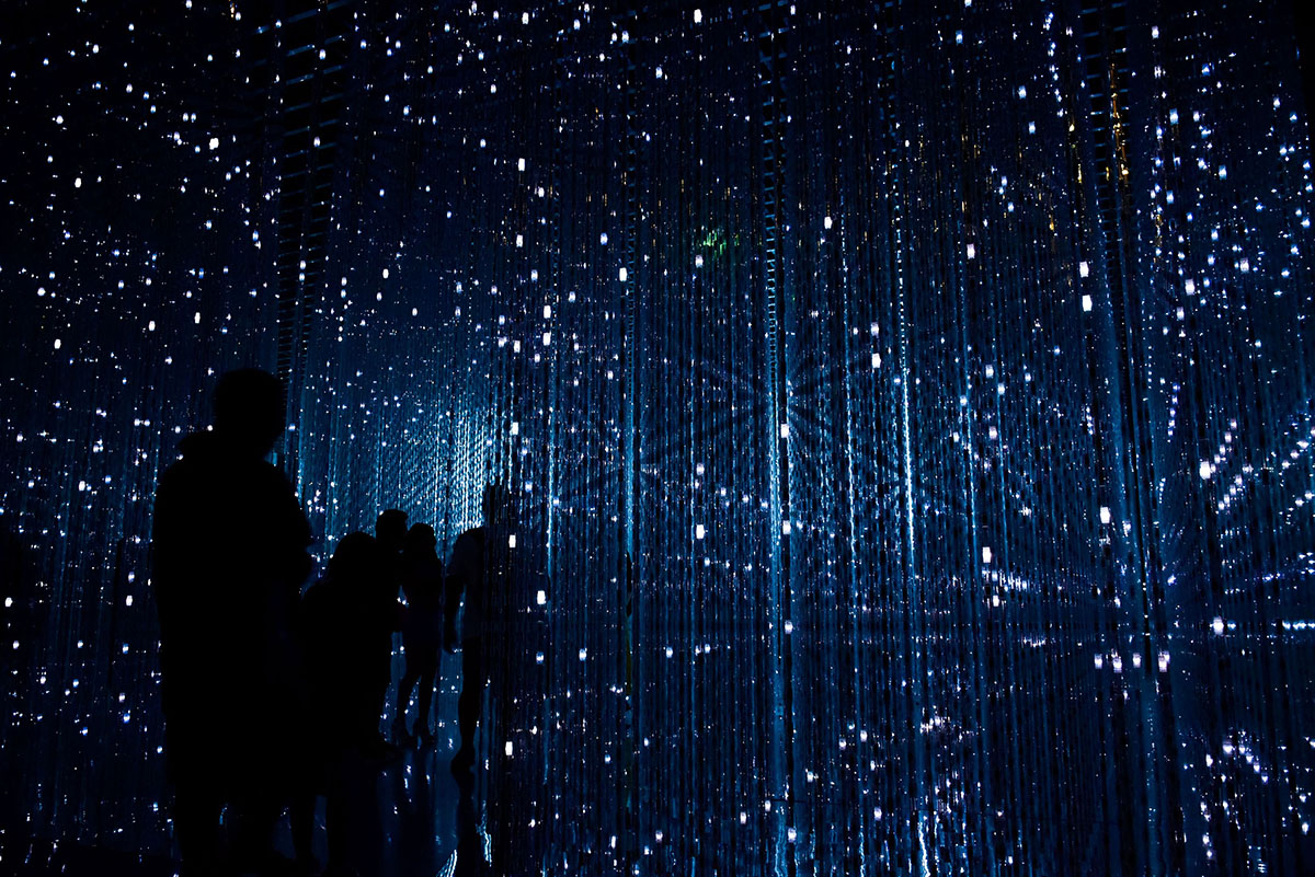 Des silhouettes se déplacent à travers une installation immersive illuminée par des milliers de petites lumières scintillantes suspendues. - Article de blog Eventdrive