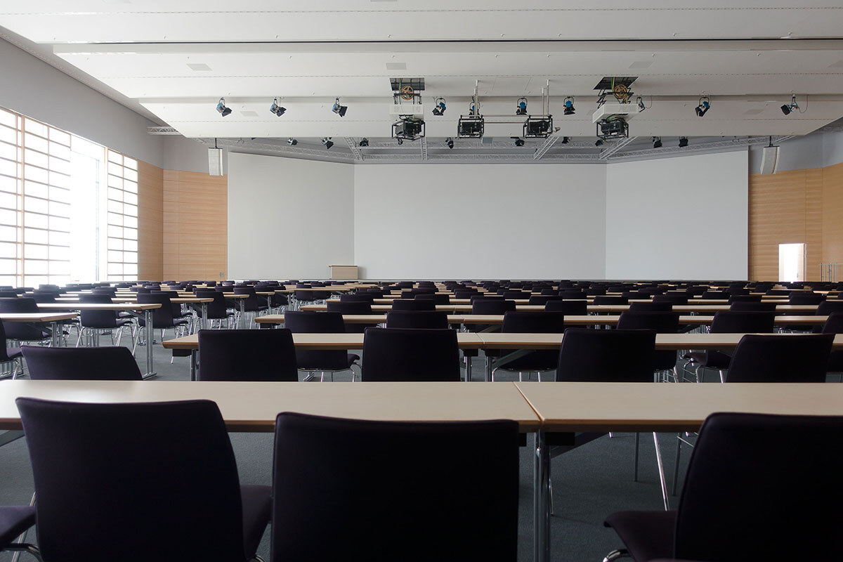 Salle de conférence spacieuse et moderne avec des rangées de tables et de chaises vides, équipée de projecteurs suspendus au plafond. - Article de blog Eventdrive