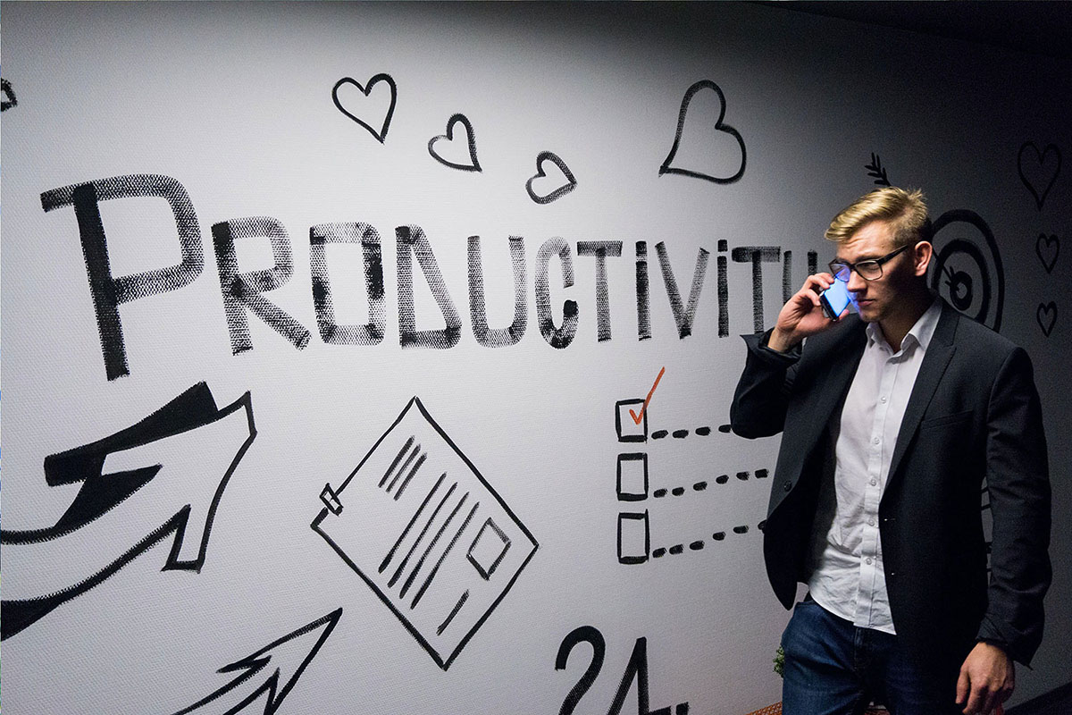 A man in a suit is talking on the phone in front of a wall decorated with drawings and the word 