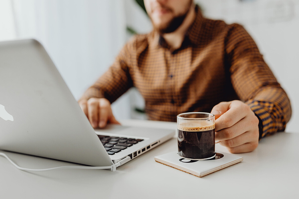 Un homme regarde son ordinateur portable, un café à la main. - Article de blog Eventdrive