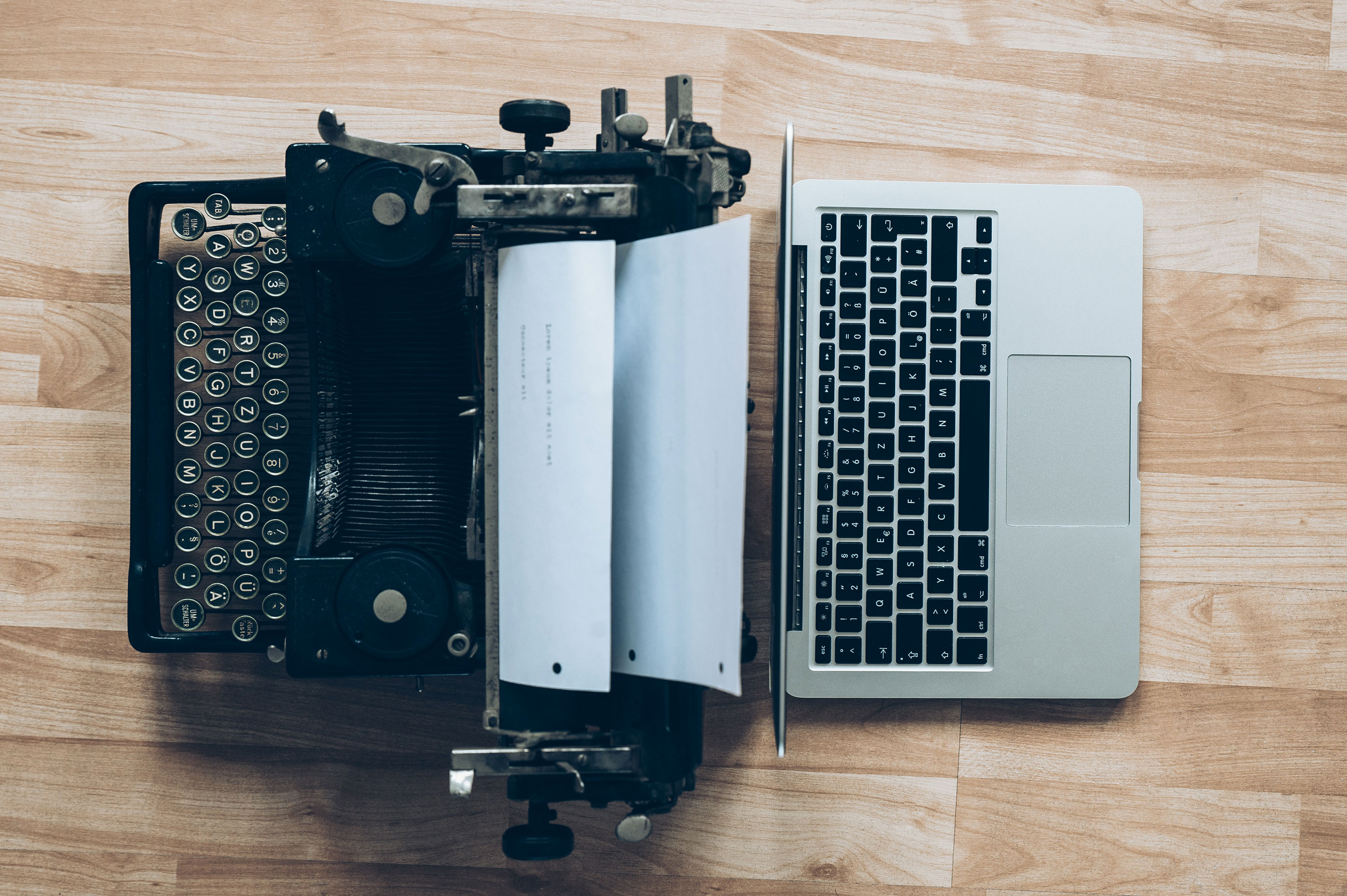 An Old Typewriter Is Placed Next to a Modern Laptop, Both Aligned Side by Side on a Wooden Floor. A Sheet of Paper Is Inserted Into the Typewriter, Creating a Strong Visual Contrast Between Old Technology and Today's Digital Tools. The Image Symbolizes the Evolution of Writing and Technology Over Time. - Eventdrive Blog Article