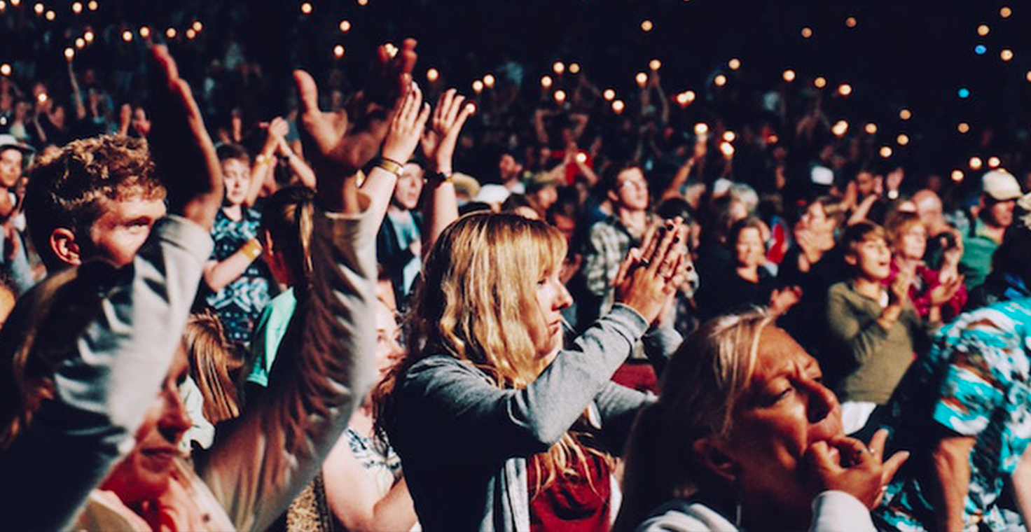 Une foule de personnes applaudissant et levant les mains lors d'un événement en plein air, éclairée par de nombreuses petites lumières à l'arrière-plan. - Article de blog Eventdrive