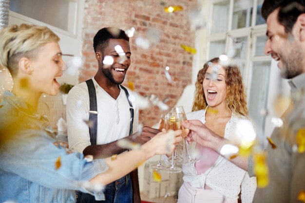 Un groupe d'amis souriants trinque avec des verres de champagne, entouré de confettis dorés qui flottent dans l'air.  - Article de blog Eventdrive