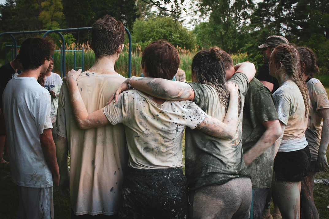 Un groupe de personnes, couvertes de boue, se tient enlacé en cercle, montrant un esprit de camaraderie et de solidarité. - Article de blog Eventdrive