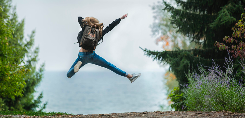 Une personne portant un sac à dos saute en l'air dans un mouvement joyeux, au milieu d'un sentier entouré de végétation. - Article de blog Eventdrive