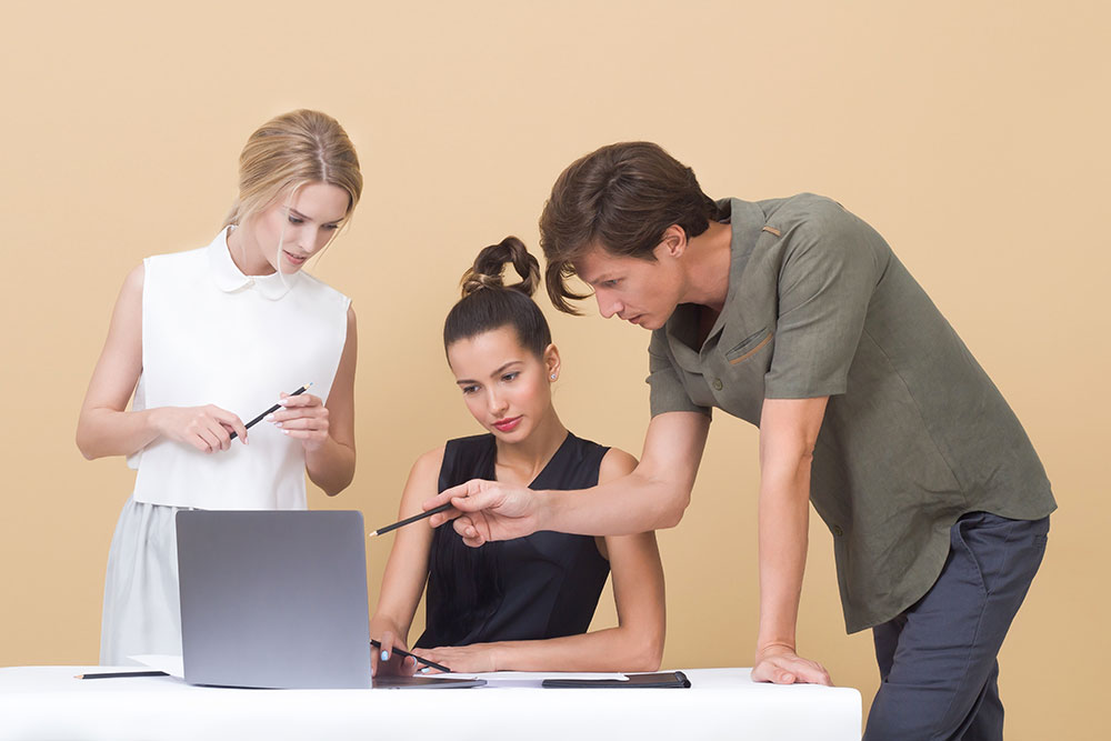 Three people working together around a laptop. A man is pointing to something on the screen with a pen, while two women watch attentively. - Eventdrive Blog Article