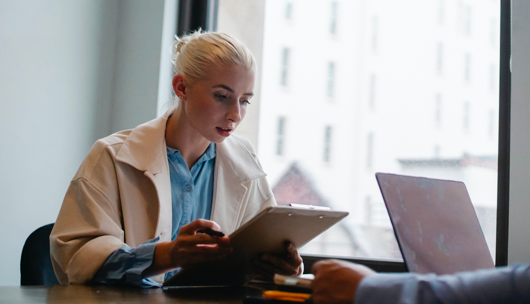 Businesswoman reviewing documents on a clipboard during a meeting in a modern office. - Blog article - Eventdrive